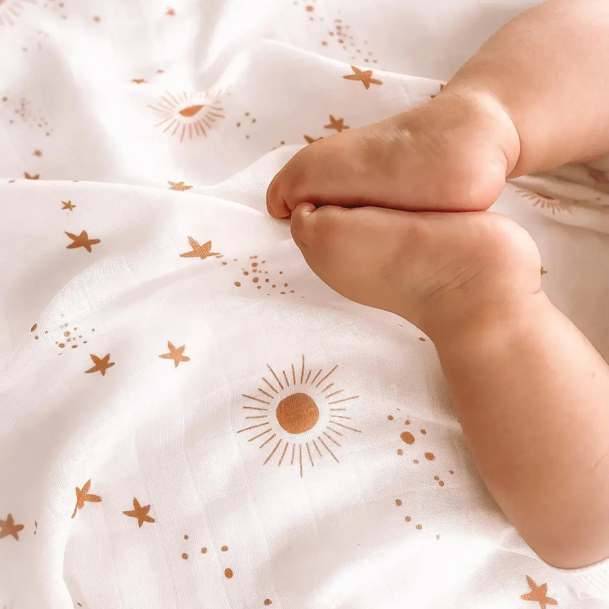 Baby's feet on a white organic muslin swaddle with a gold star and sun constellation print