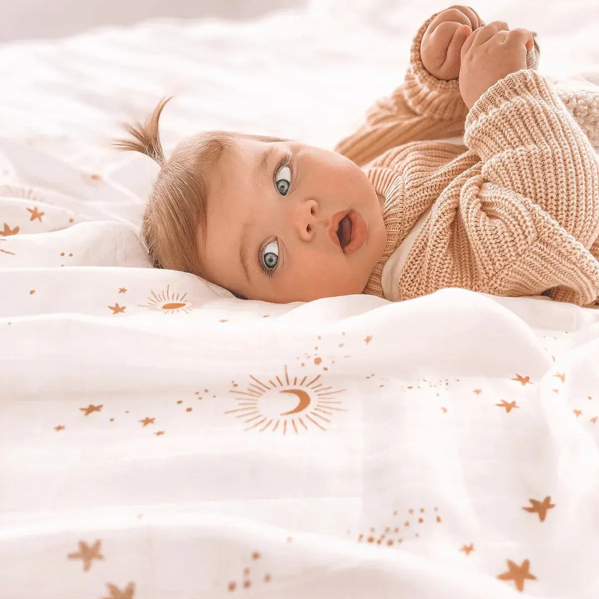 Baby lying on a white gender neutral swaddle with gold stars, suns and moons scattered across it