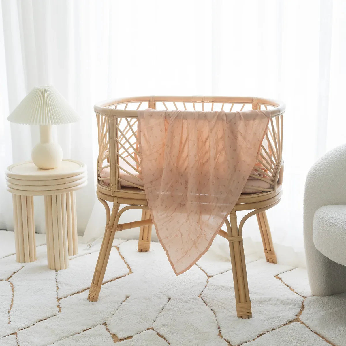 Pink foliage print muslin swaddle hanging in a styled nursery
with rattan bassinet, Fox and Fallow