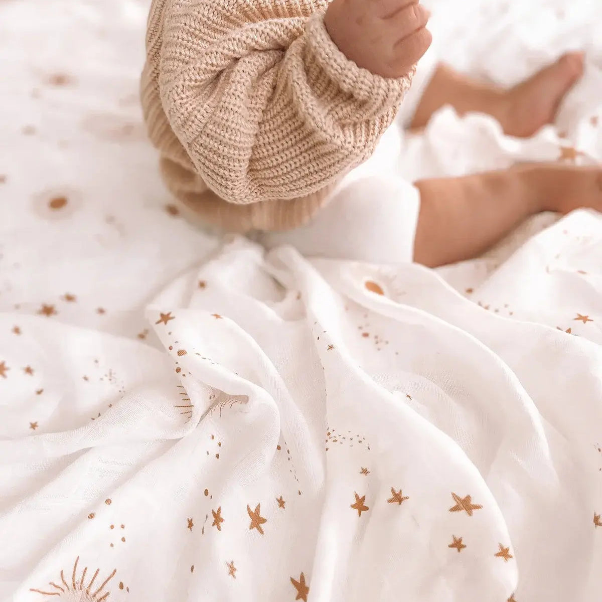 Close up of a baby sitting on an organic muslin swaddle with a star print