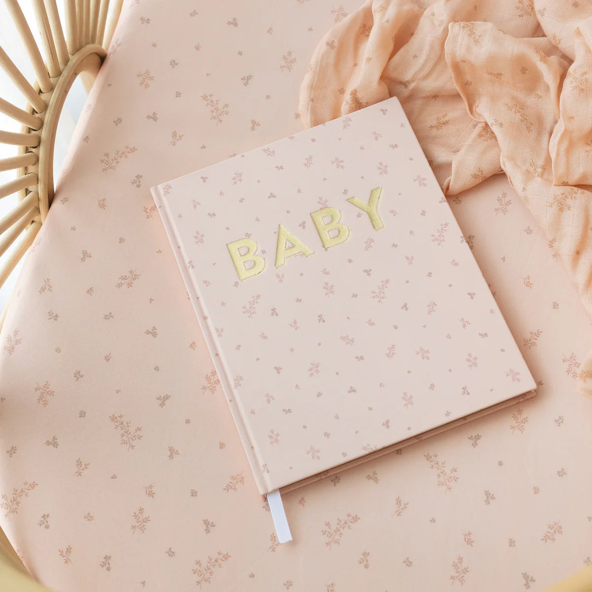 Pink BABY memory book and Wild Ruscus organic muslin swaddle styled on a wicker nursery bassinet
