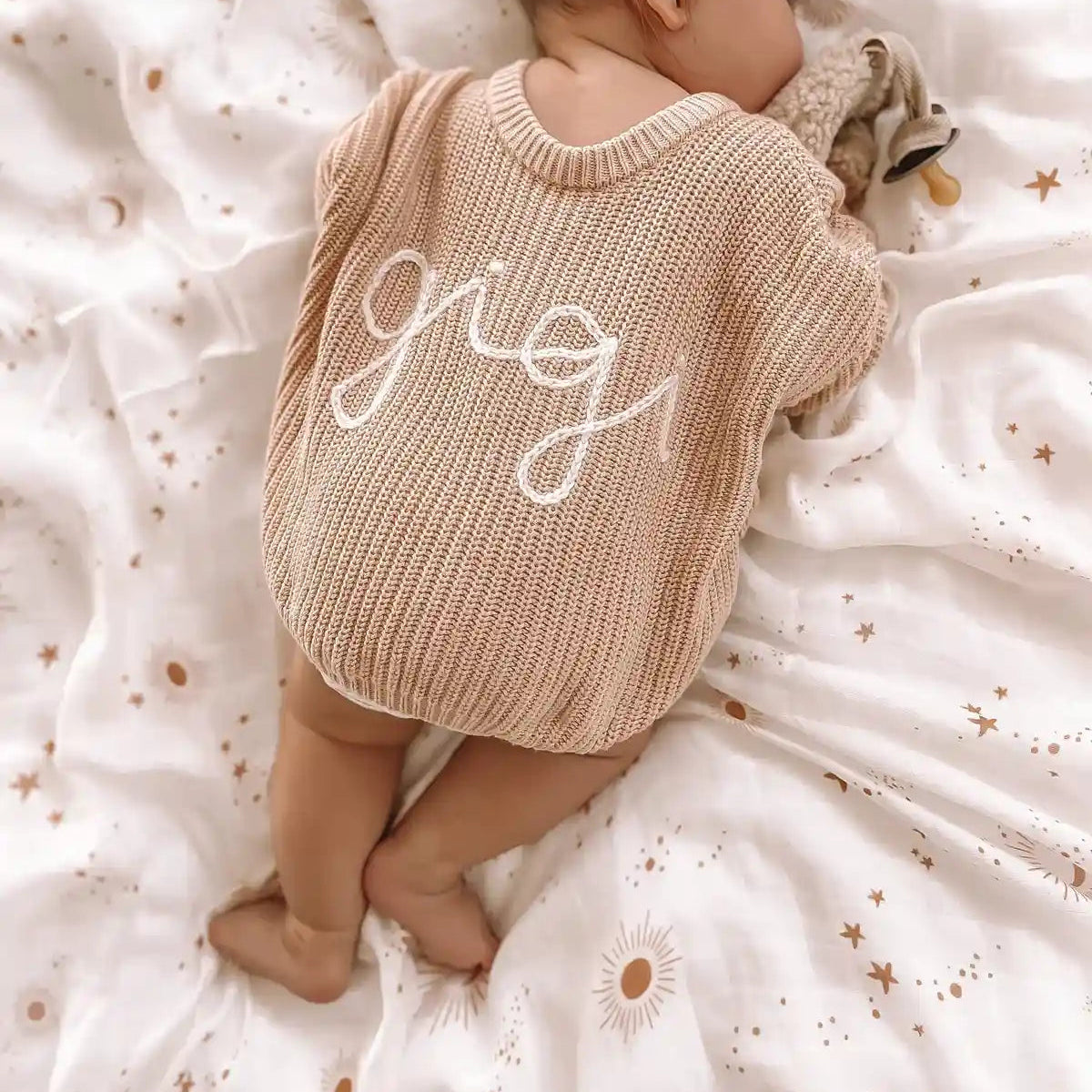 Baby in a personalised knit jumper lying on white Constellation star print swaddle
